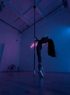 a woman standing on top of a pole in the middle of an empty room with neon lights