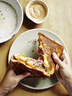 a person holding a sandwich in their hand on a plate next to bowls of soup