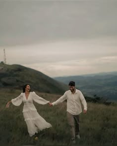 a man and woman holding hands while walking through the grass on top of a hill