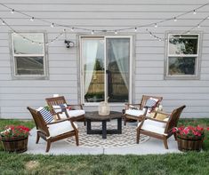 a patio with chairs, table and potted plants on the grass outside in front of a house