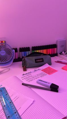 a desk with pens, pencils and markers on it next to a pink light