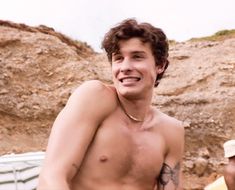 a shirtless young man standing in front of a rock formation with two other men