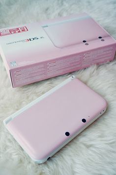 a pink nintendo 3ds sitting on top of a white fur covered floor next to a box