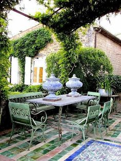 an outdoor dining area with green chairs and blue vases on the table, surrounded by greenery