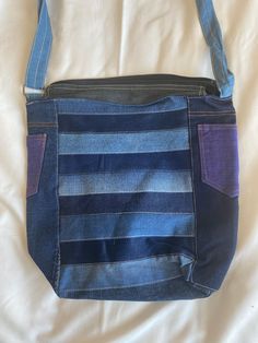 a blue and purple striped purse sitting on top of a bed next to a white sheet