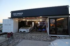 two cars are parked in front of a garage with their doors open and people standing outside