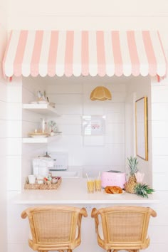 two chairs sitting under a pink and white awning next to a counter with pineapples on it