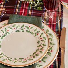 a christmas place setting with holly and red berries on the plate, napkins and silverware