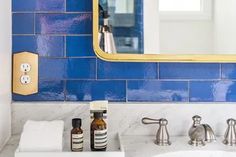 a bathroom with blue tile and gold trim on the mirror, sink, and soap dispenser