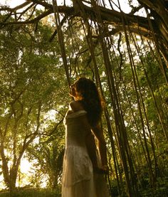 a woman is standing in the woods with her back to the camera and looking up