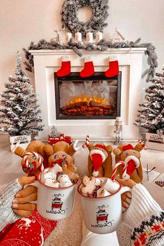 two people holding mugs with teddy bears in front of a fireplace decorated for christmas