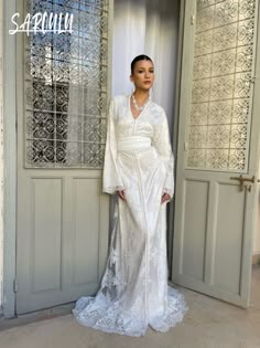 a woman standing in front of an open door wearing a white dress and pearls necklace