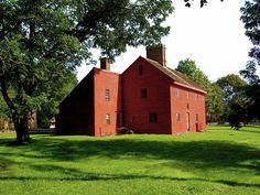 an old red brick house sitting in the middle of a lush green field next to trees