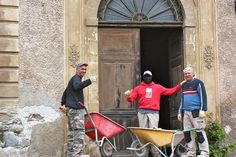 three men standing in front of a door with a wheelbarrow