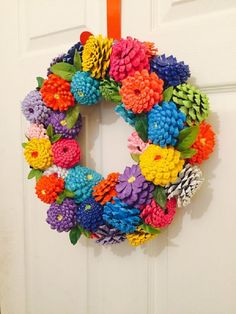 a colorful wreath hanging on the front door with pine cones and flowers attached to it