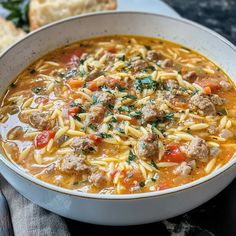 a white bowl filled with pasta and meat soup on top of a table next to bread