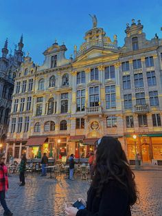 people are standing in front of an old building at dusk with the sun setting on it