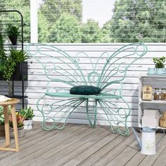 an outdoor patio area with potted plants and a metal butterfly bench on the deck