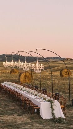 a long table is set up in the middle of an open field with chandeliers