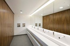 a long white counter top in a bathroom with wooden cabinets and mirrors on the wall