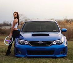 a woman standing next to a blue car holding a frisbee in her hand