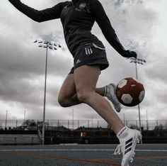 a woman kicking a soccer ball on top of a field with sky in the background