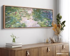 a painting hanging on the wall above a dresser with books and flowers in vases