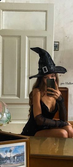 a woman in a witch costume taking a selfie with her cell phone while sitting on the floor