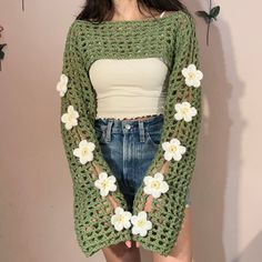 a woman standing in front of a wall wearing a green sweater with flowers on it