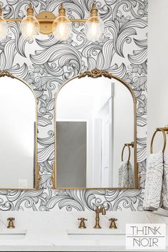 a bathroom vanity with two mirrors and lights on it's sides, in front of a wallpapered background