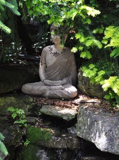 a buddha statue sitting on top of a rock next to a forest filled with green plants