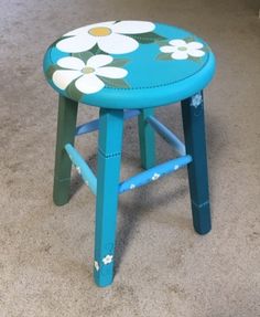 a blue stool with white flowers painted on the top and bottom, sitting in a room