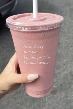 a person holding up a pink smoothie with a straw in it's cup