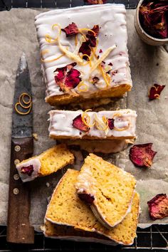 slices of cake with icing and dried rose petals on the table next to a knife