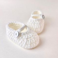 a pair of white crocheted baby shoes with button on the front and bottom