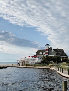 a house on the water with a dock in front of it and some buildings near by