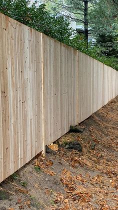 a wooden fence in the middle of a park with leaves on the ground and trees behind it