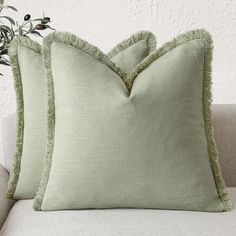 two green pillows sitting on top of a white couch next to a vase with flowers