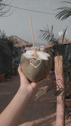 a person holding up a coconut drink with a straw in the shape of a heart