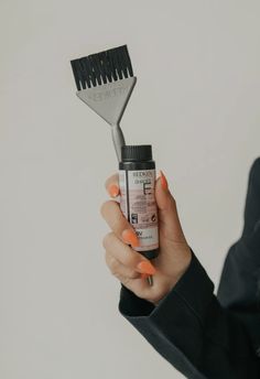 a woman holding a brush and comb in her hand with orange nail polish on it