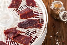 slices of raw meat are on a white tray next to spices and seasoning in glass jars