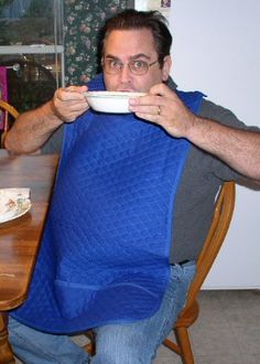 a man sitting at a table with a blue bib around his neck eating from a bowl