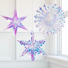 two snowflakes hanging from strings in front of a window with white walls