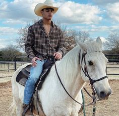 a man sitting on top of a white horse wearing a cowboy hat and blue jeans