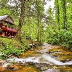 a red house sitting on top of a lush green hillside next to a river in the forest