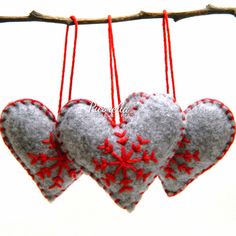 three felt hearts hanging from a tree branch with red thread and snowflakes on them