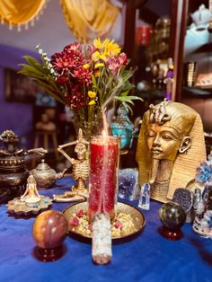 a table topped with vases filled with flowers next to an egyptian mask and other items