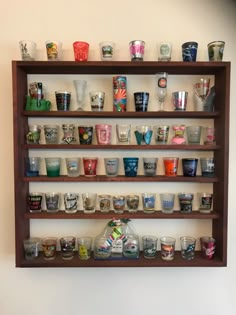 a wooden shelf filled with lots of glasses on top of a wall next to a white wall