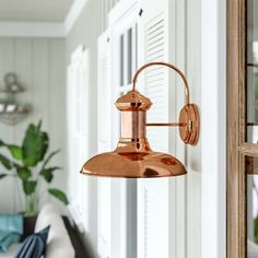 a copper light hanging from the side of a white wall next to a blue chair