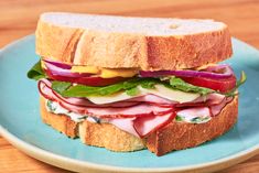 a sandwich with meat, lettuce and cheese on a blue plate sitting on a wooden table